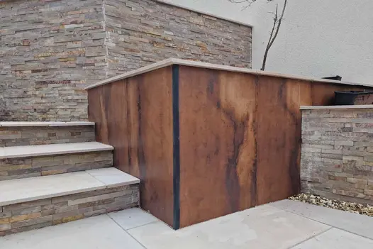Deep terraced beds, one faced with Siena Copper 1200x600 DesignClad, next to 3 steps with stone-clad risers to match other beds.