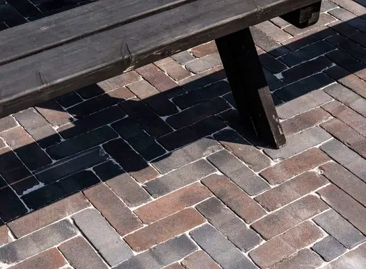 Wood pub bench casts shadow on Ancona clay pavers laid in herringbone pattern with sanded joints.