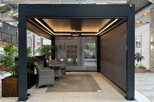 Deluxe Anthracite Grey Metal Pergola in a showroom with the blinds half up half down and integrated lighting and heating on, creating a cosy ambiance.