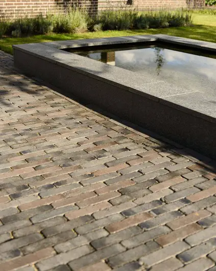Rectangular pond with wide coping next to stretch of paving of Ancona clay pavers laid running bond. Lawn in background.