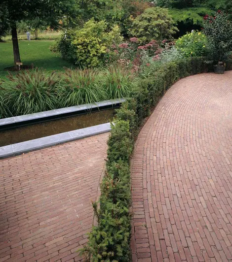 Roma Brick Paving laid in 2 separate patio areas, with the dutch clay pavers meeting at a hedge in the middle, densely planted lawn in background.