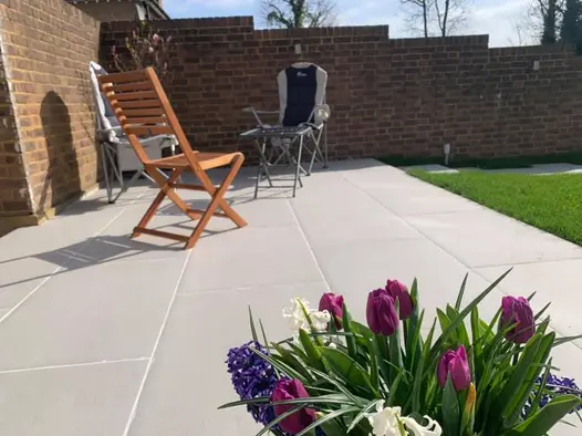 Florence Grey porcelain patio laid in corner of walled garden, seen over pot of purple tulips. Design by A and G Gardening.