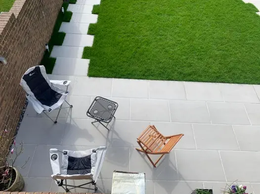 Staggered Florence Grey porcelain path leads to patio with folding chairs and table in corner of walled garden, viewed from above.