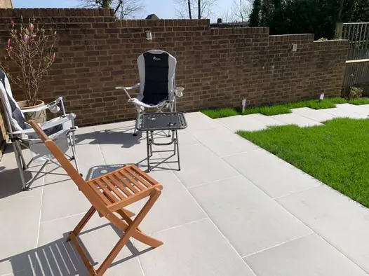 Florence Grey porcelain tiled path leads along lawn edge to paving with folding chairs and table. Design by A and G gardening.