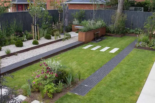Corten steel planters with lush green and purple plants, approached by an Amersham clay paver path with light pebbles on the left side.