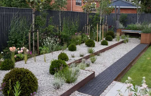 Corten steel planters filled with green and purple plants, with an Amersham clay paver path leading to them and light pebbles on the left.