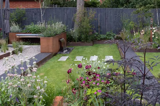 2 paths of Amersham clay pavers leads to Corten steel planter waterfeature overflowing with green and purple plants and flowerbeds.