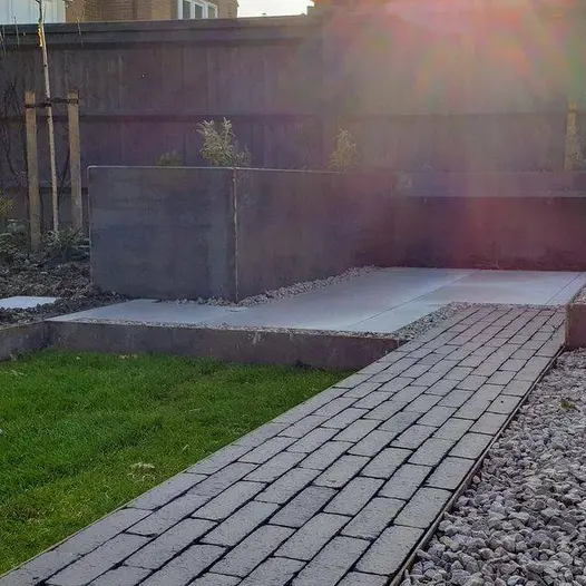 An Amersham clay paver path, flanked by light pebbles on the right, leads to patio and Corten steel planters.