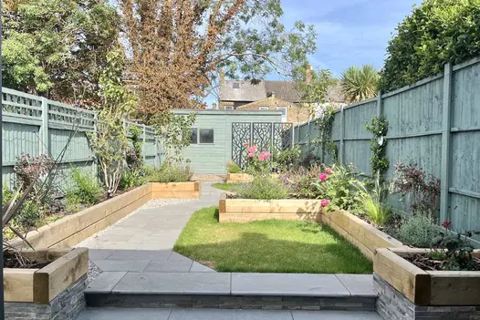 Bullnose outdoor steps lead up to path paved in graphite grey limestone paving, with interspersed lawn and raised flowerbeds.