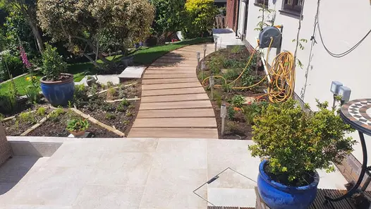 Curved rovere porcelain stepping stone path leading from a patio to the back door of a white rendered house.