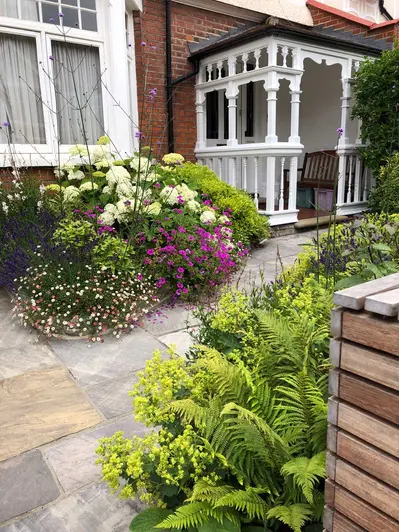 Front garden of Edwardian terraced house with Tumbled Black sandstone paving slabs leading between planted beds to wooden porch.