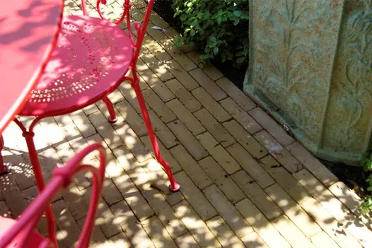 Red metal bistro chair sits on Westminster Clay Pavers, with ornate planter on adjacent border. Design by Amelia Bouquet.