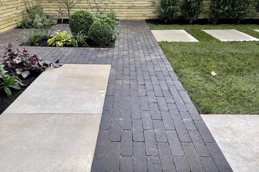 Amersham clay pavers laid with pale paving slabs, with inset beds and slatted fence, next to lawn. Built by Bark Brick and Block.