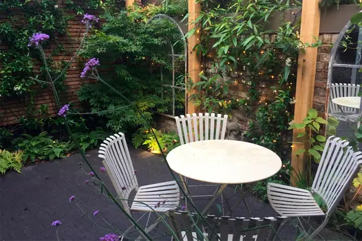 Small garden featuring two window-style mirrors with plants climbing the brick wall they hang from, and metal furniture on an Amersham clay paver patio.