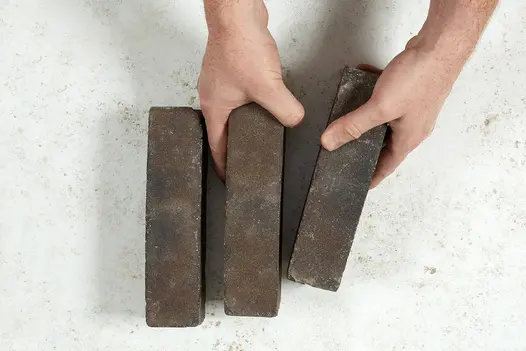 2 hands place 2 dark brown and grey Ancona clay pavers next to a 3rd against a light background. Free UK delivery available.