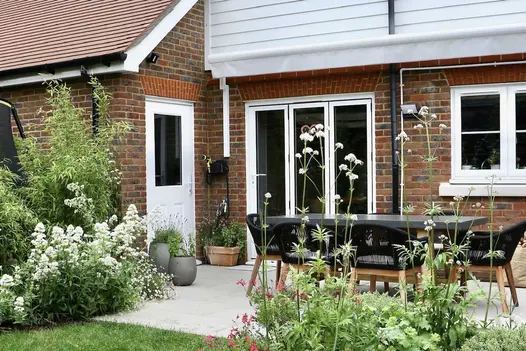 Back garden on a sunny day in the height of summer looking towards a red bricked house with a Porcelain patio and dining set.