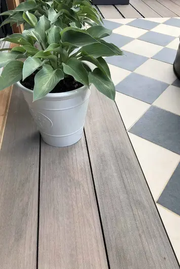 Close view of Traditional Designboard Composite Decking with ceramic plant pot sitting, mosaic tiles to the right.