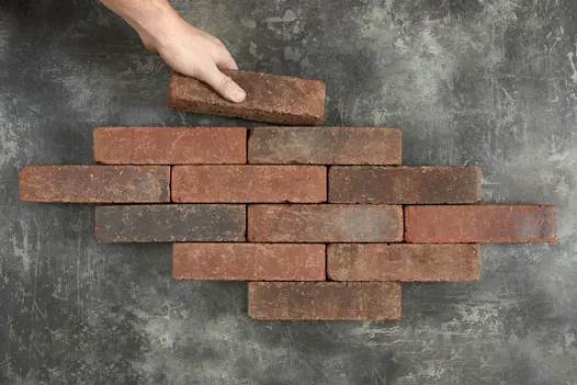 Hand places an Antique Red Clay Paver at top of 11 other bricks arranged in rows of 1, 2 and 3. Free UK delivery available. 