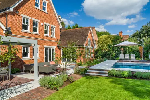 Antique Red clay paver and Dove Grey sawn sandstone patio, with pergola and garden furniture, borders steps up to swimming pool.