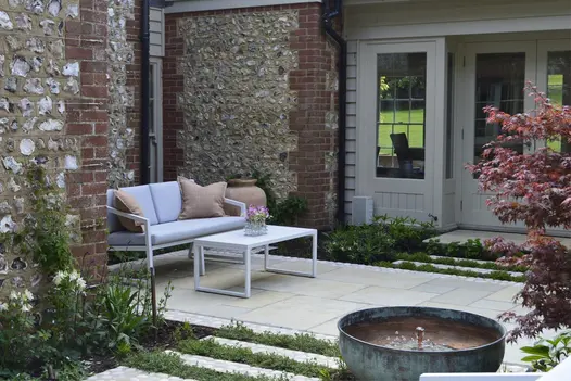 French windows of house with flint-knapped walls net to patio strip of Antique Yellow limestone slabs with outdoor sofa and table.