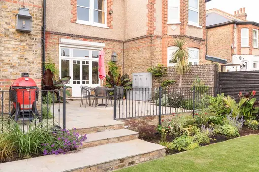 Antique Yellow Limestone steps with Cotswold Belgian brick risers ascend to patio outside french doors, with railings and planting.