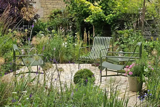 Four green metal armchairs sit in a circle made of Mint Sandstone Setts with trees, shrubs and greenery surrounding.
