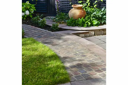 Curved path of Autumn Brown Sandstone Setts with lawn and patio either side, leads to flowerbed and plant pot.