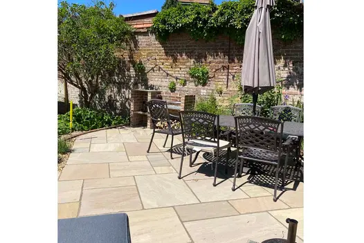 Dining set arranged on a Raj Green Indian sandstone patio, framed by a brick wall, a brick barbeque sits next to the dining area.