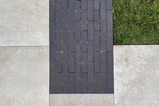 View from above of strip of Amersham dark grey clay pavers laid between pale paving slabs and lawn. Design by Bark Brick and Block.