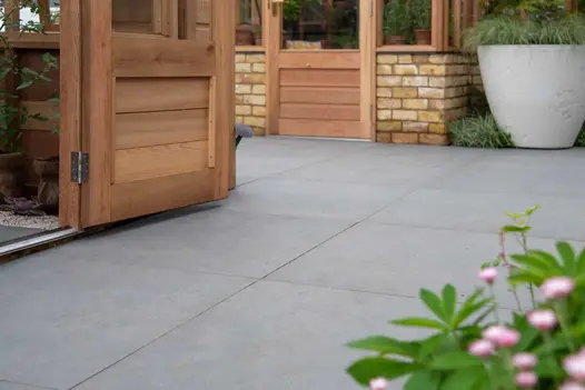 Anthracite Large Format Porcelain Paving laid between 2 greenhouses and large white planter with grasses. Built by Base Squared.