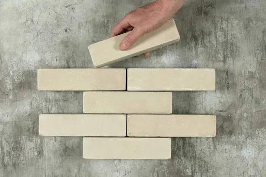 Hand places 1 Beige stone paver into formation of 6 other patio bricks arranged in rows of 1 and 2. Free UK delivery available.
