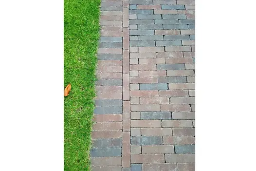 Soldier course of bricks edges dry Bergamo clay paver path laid running bond, showing red and black colours, nest to mown grass. 