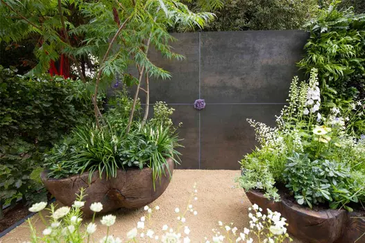 Wall faced with 4 panels of Steel Dark DesignClad. Violet joints meet at matching roundel. Large planted pots to either side.