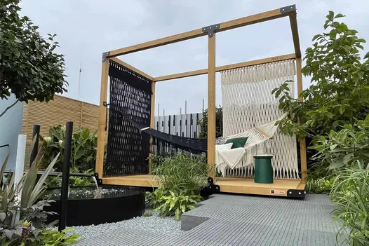 Hammock hangs in wooden frame which partially sits on Black granite paving with bespoke grooves, between beds with exotic planting.