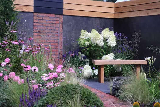 Brick path curves between planted colourful bed and Black granite paving treated with colour-enhancer at RHS Tatton Park.