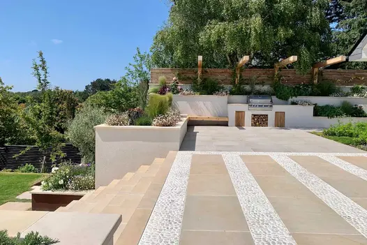 Steps descend to lawn from wide terrace paved with Harvest smooth sandstone slabs and cemented-in pebbles. Outdoor kitchen on far wall.