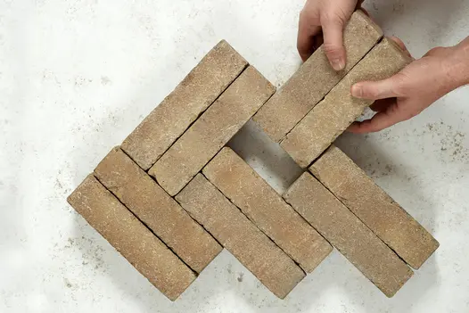 2 hands add 2 bricks to 8 Westminster Clay Pavers in double herringbone pattern on light background. Free UK delivery available.