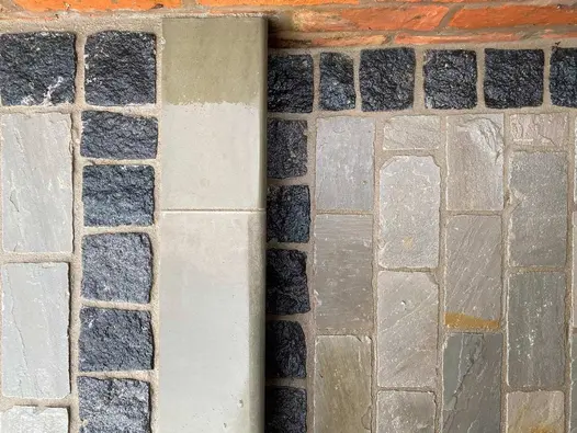 Natural black granite setts, laid between buff-colored stones wet from rain, lead to a bullnose step that ascends to the patio.