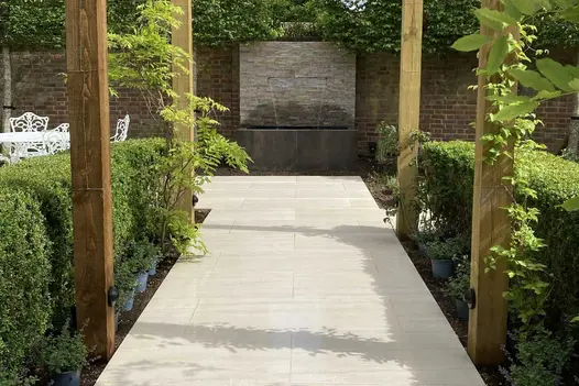 Path between hedges and wooden posts leads to wall where water spout empties into trough faced with Steel Dark external cladding.