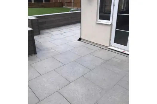 Astor Grey porcelain paving patio with slot drain wraps around corner of white house. Built by C Howell Builders and Landscapers.