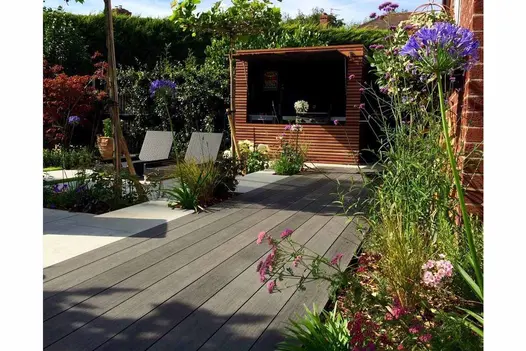 Charcoal Designboard composite decking separates planted border from paved area with 2 loungers edged by hedge and slatted screen.