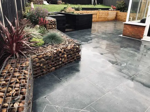 Multi level back garden with a Charcoal porcelain patio in the lower section and a lawn on the upper section.