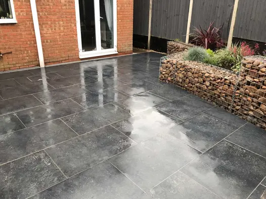 Red brick house with charcoal porcelain patio leading directly from the patio doors and raised beds made from filled gabion cages.