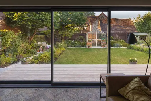 View from window shows quaint garden at dusk with sun setting over building, limed oak millboard seen in front of lawn.