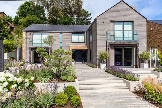 Cinder porcelain pathway and matching steps with flower beds on both sides leading towards a timber clad house.