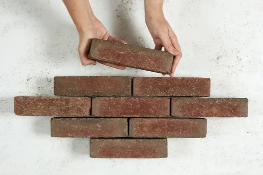 Hand adds 9th stone paver to 8 Winton clay pavers arranged in 4 rows in lozenge shape. Free UK delivery available.