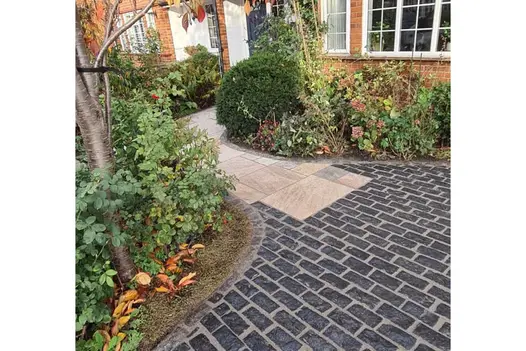 The natural black granite setts taper to seamlessly join the stone slab path in the front garden of a period suburban house.