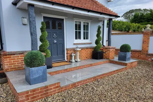 Alongside paving steps, Wet Florence Storm Porcelain Paving leads up to the front door, with topiary planting adorning either side.