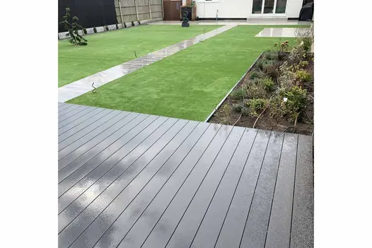 Lawn split in two with porcelain path leads to decking area using dark ash brushed composiye decking, shown in wet UK weather.