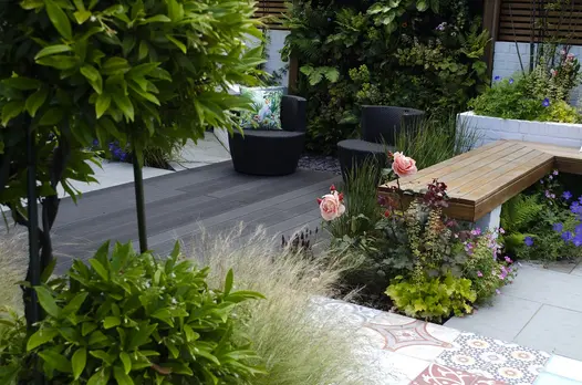 Charcoal composite outdoor decking laid with decorative tiles in garden with topiarised laurel, living wall and brick raised beds.